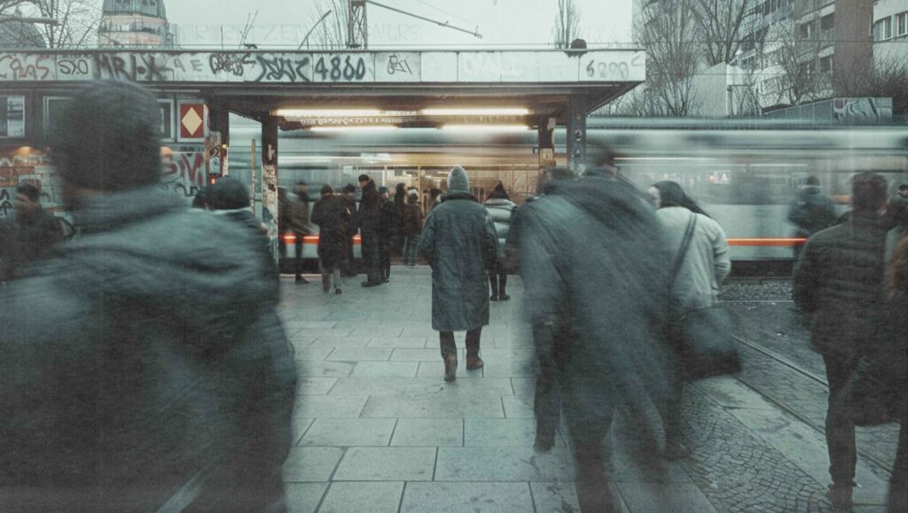 Menschen laufen über einen Platz Richtung Bahnsteig, im Hintergrund fährt eine Bahn vorbei.