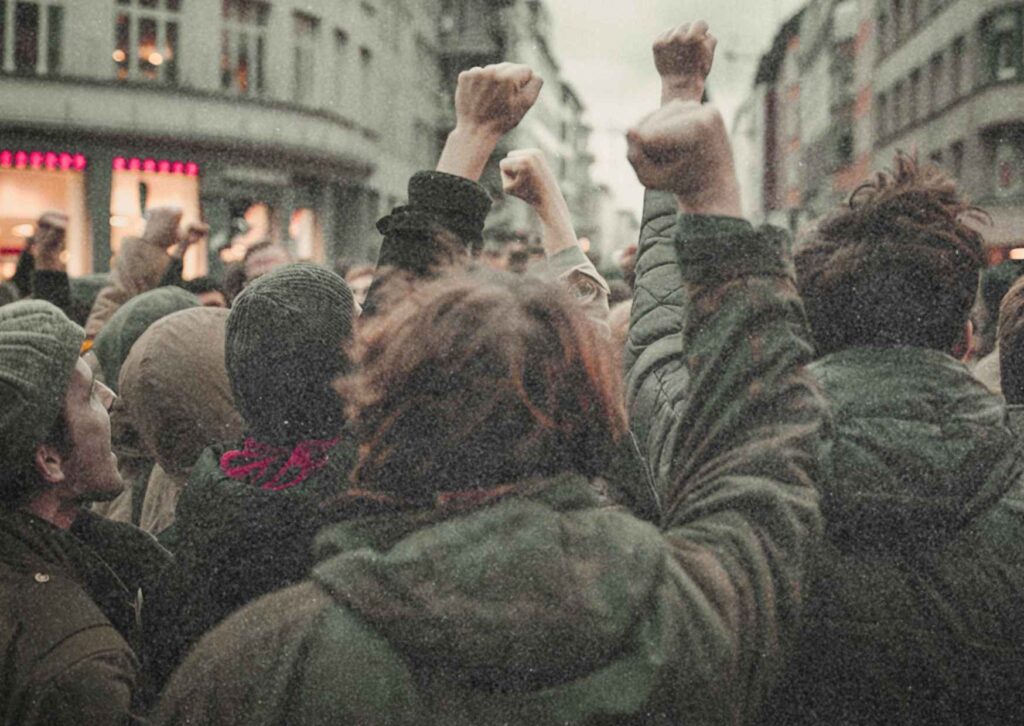 Foto mehrerer Personen von hinten, einige mit erhobener Faust, die offenbar gegen etwas protestieren.
