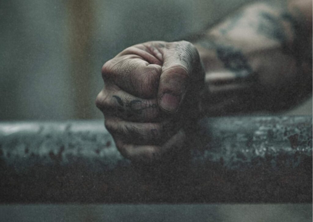 Tätowierte Faust an einem rostigen Gitter – Symbol für Gefängnis und Widerstand