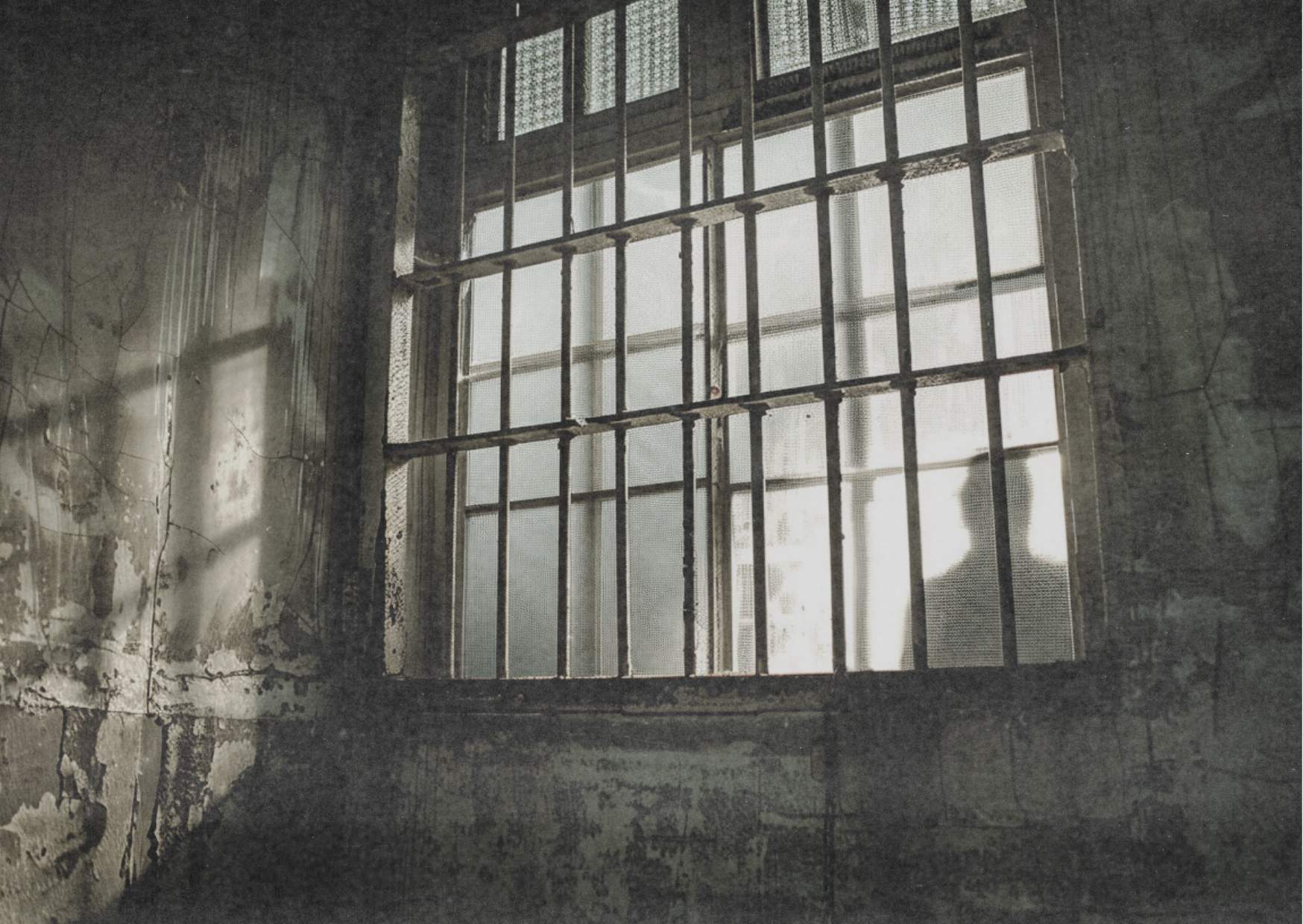 Silhouette einer Person hinter Gitterfenster mit Lichteinfall – symbolisch für Gefängnis, Isolation und Strafsystem.