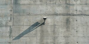Eine einzelne Überwachungskamera an einer Betonwand, die einen langen Schatten wirft.