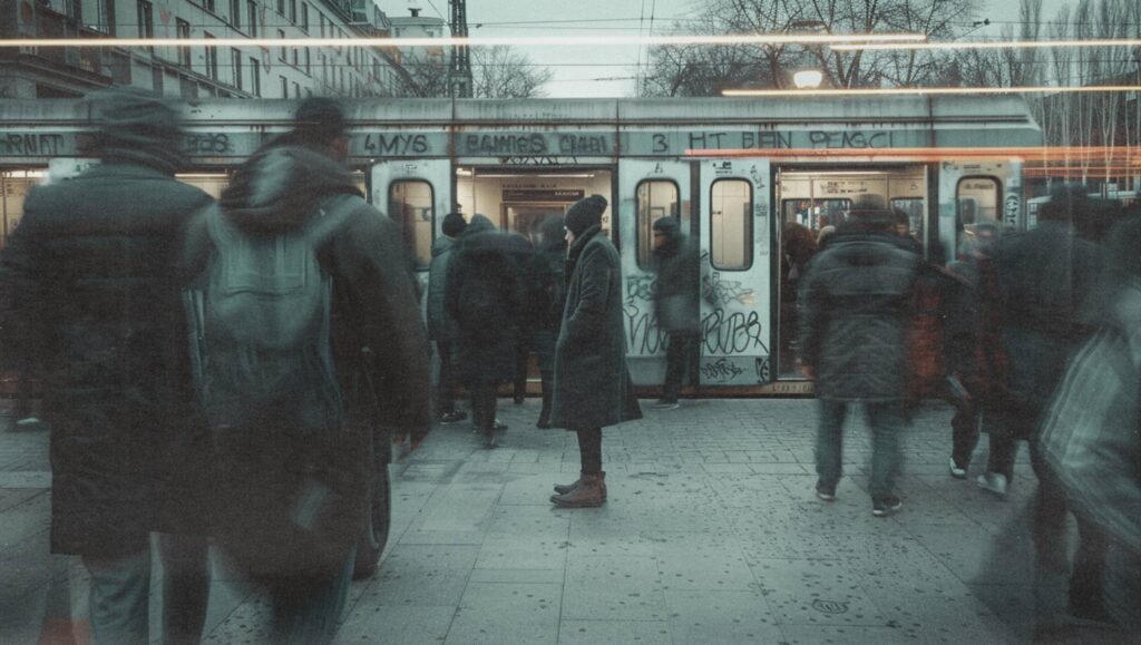 Person steht allein am Bahnsteig, während Menschen um sie herum vorbeihasten – Symbol für Orientierungslosigkeit und gesellschaftliche Verunsicherung.