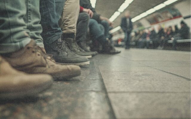 Menschen warten am Bahnsteig – Nahaufnahme der Schuhe, unscharfer Hintergrund