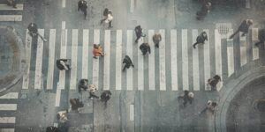 Menschen gehen in unterschiedlichen Richtungen über einen Zebrastreifen in einer europäischen Innenstadt. Die Szene wirkt alltäglich und zeigt anonymisierte PassantInnen im öffentlichen Raum.