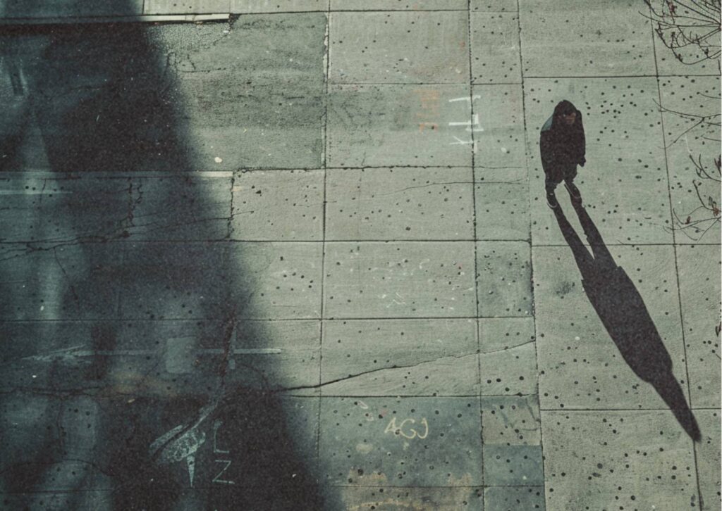 Person mit langem Schatten auf einer urbanen Betonfläche – Symbol für berufliche Rollen und Zuschreibungen.